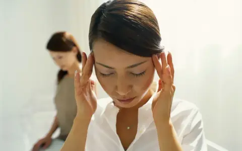Kobieta zamyka oczy, masując skronie. Czy to skutki uboczne kwetaplex? W tle druga kobieta.