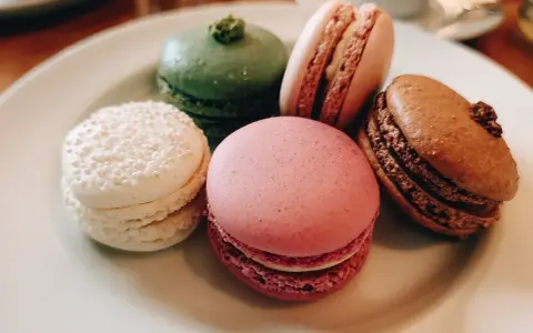 Fem färgglada macarons på en tallrik. En vit med pärlor, en grön, en rosa, en ljusrosa och en brun. Perfekt för ett macarons recept.