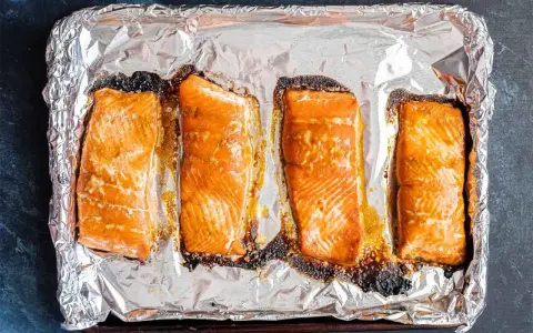 Cztery kawałki łososia pieczone na folii aluminiowej, gotowe do przygotowania sushi.