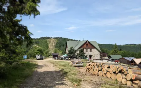 Kamienna chata i stosy drewna przy szlaku na Klimczok. W tle widać górę z wytyczonymi ścieżkami i las.