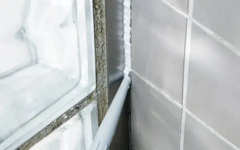 En fogpistol applicerar ny silikonfog längs en vägg av grå kakelplattor och glasblock.