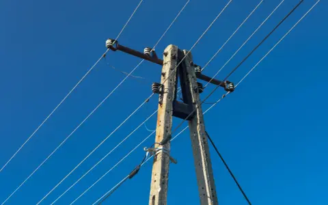Słup energetyczny z przewodami na tle błękitnego nieba. Zastanawiasz się, ile wynosi odszkodowanie za słupy energetyczne na działce?