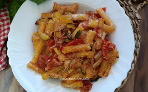 Piatto di pasta con zucchine e pomodorini, condita con formaggio grattugiato e basilico fresco.