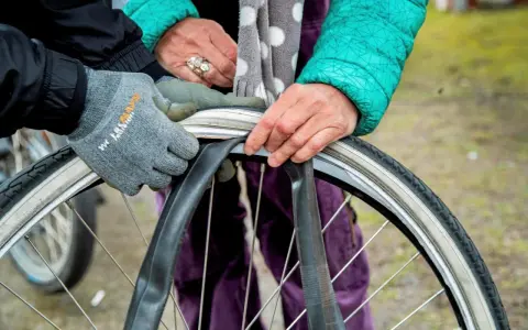 Två personer byter cykelslang. En med grå handske och en med grön jacka och prickig scarf.
