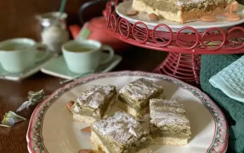 Carrés de croute à thé aux amandes, saupoudrés de sucre glace, servis avec des tasses de thé vert.