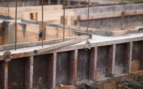Drewniany szalunek czeka na beton. Widać zbrojenie i świeży beton.