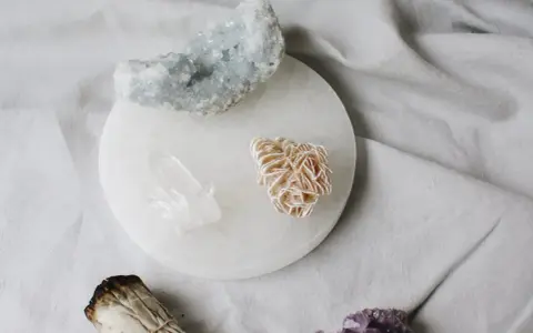 Cristales de selenita, cuarzo y amatista sobre un plato de selenita, junto a un manojo de salvia. Guía para saber como limpiar la selenita.