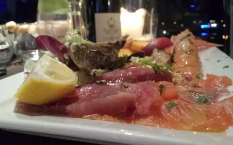 Un piatto di pesce crudo, con salmone, tonno e scampi, accompagnato da limone e insalata. Un'ottima occasione per degustazioni gastronomiche.