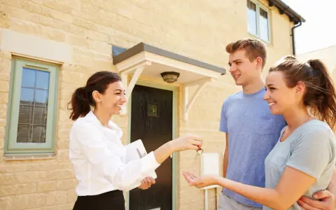 Une agent immobilier remet les clés d'une maison à un jeune couple. Ils sont heureux d'acquérir leur nouveau logement, peut-être grâce au droit de préemption locataire.