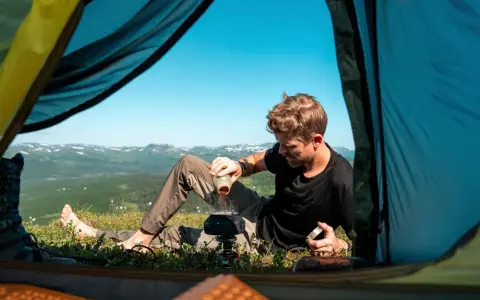 Man förbereder kaffe utanför tältet med en fantastisk utsikt. En del av packlista vandring sommar.
