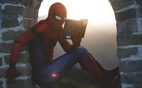Spider-Man w czerwonym stroju siedzi na murze i czyta książkę. Czy komiks to utwór literacki? Nawet superbohaterowie potrzebują chwili wytchnienia i wiedzy.