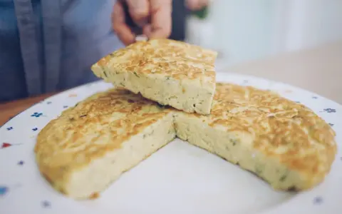 Una fetta di frittata, preparata con la ricetta perfetta, viene sollevata da un piatto decorato.