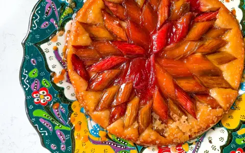 Owoce pod kruszonką, czyli tarta tatin z rabarbarem, błyszcząca od karmelu, na kolorowym, zdobionym talerzu.