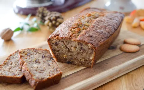 Un délicieux cake banane, coupé en tranches, sur une planche en bois. Des noix et des biscuits complètent cette gourmandise.