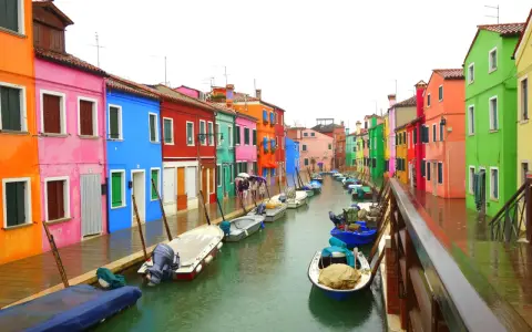 Venise : une maison colorée et d'autres maisons aux teintes vives bordent un canal où flottent des bateaux.