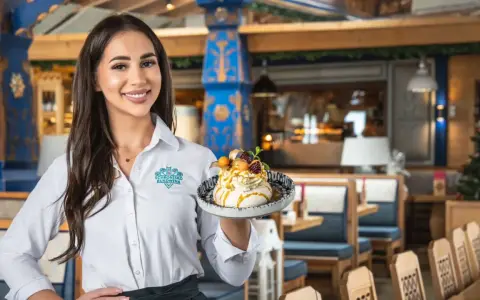Kelnerka prezentuje deser z menu Schroniska Smaków Bukowina. Wnętrze restauracji zdobią góralskie wzory.