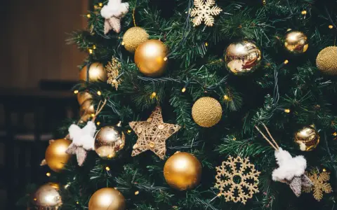 Un albero di Natale addobbato con palline dorate, fiocchi di neve scintillanti e stelle di stoffa. Le luci gialle creano un'atmosfera magica, un vero simbolo albero di natale.