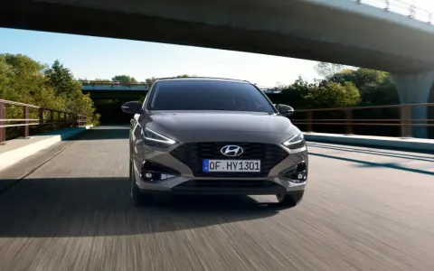 Szary Hyundai i30 1.4 benzyna pędzi po drodze pod mostem, otoczony zielenią.
