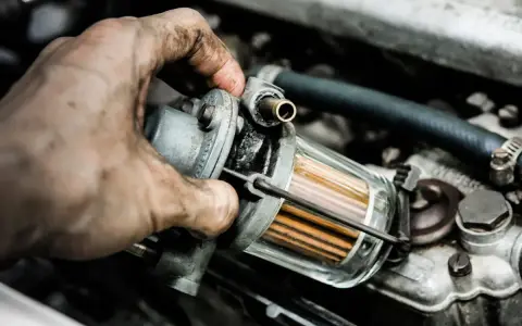 Brudna ręka mechanika wymienia filtr paliwa, by wyeliminować nierówną pracę silnika na wolnych obrotach LPG.