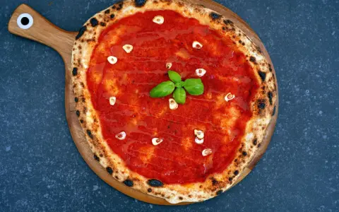 Eine klassische Pizza Marinara mit Tomatensauce, Knoblauch und frischem Basilikum auf einem Holzbrett.