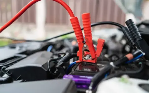 Czerwone kable rozruchowe podłączone do akumulatora samochodowego. Dowiedz się, jak dobrać prostownik do akumulatora, by uniknąć problemów.