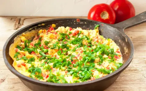 Pyszny omlet z warzywami, posypany szczypiorkiem, gotowy do podania. Obok leżą dwa pomidory.