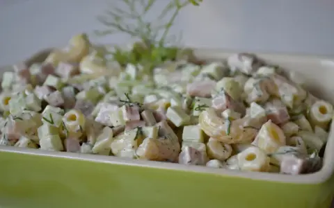 Pyszna sałatka z makaronem, szynką, ogórkiem i serem, udekorowana świeżym koperkiem.