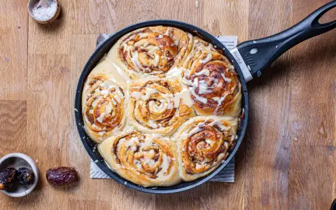 Frisch gebackene Zimtschnecken mit Apfelstückchen und Zuckerguss in einer Pfanne. Ein köstliches Apfel Zimtschnecken Rezept zum Nachbacken.