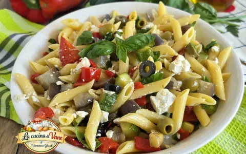 Pasta fredda con feta, peperoni, zucchine, melanzane e olive nere. Un piatto estivo colorato e saporito.