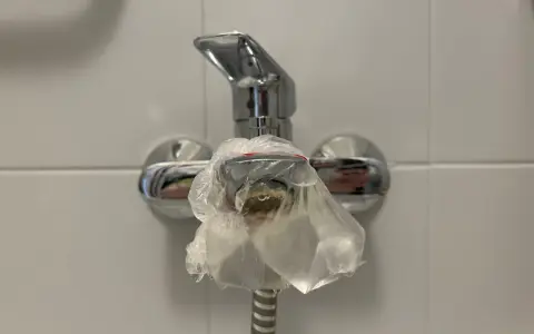 Krople wody spływają z baterii, na której zawiązano woreczek. To metoda, jak wyczyścić sitko w baterii kuchennej.