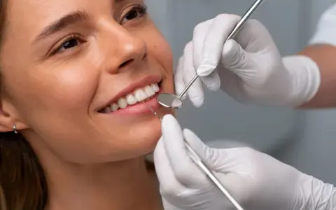 Uśmiechnięta kobieta podczas badania stomatologicznego. Dentysta sprawdza zęby, by upewnić się, że bonding nie niszczy zębów.