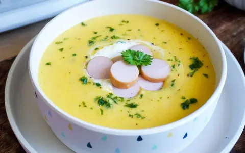 Cremige Kartoffelsuppe, zubereitet im Thermomix, garniert mit Würstchenscheiben, einem Klecks Sahne und Petersilie.