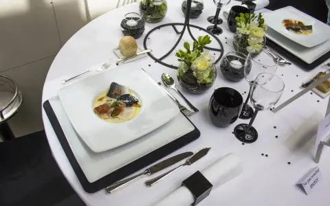 Une table de restaurant dressée avec élégance, un plat de poisson en vedette, des verres noirs et des fleurs.