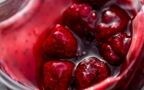 Gros plan sur des framboises dans un liquide rouge vif, parfait pour un nappage framboise facile et gourmand.