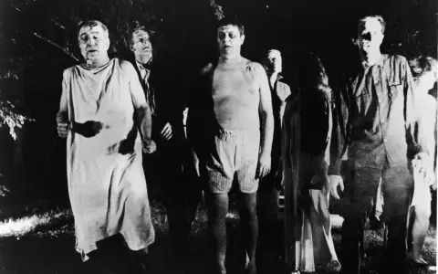 Un gruppo di persone dall'aspetto spettrale, un'immagine che evoca il significato di un b movie, cammina in un bosco di notte.