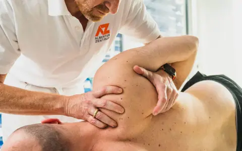 Therapeut führt eine gezielte Massage bei Schulterschmerzen durch. Hände des Therapeuten bearbeiten den Schulterbereich eines liegenden Patienten.