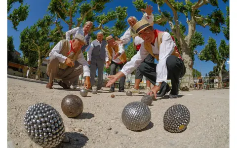 Des hommes jouent à la pétanque sous les platanes. La question "la pétanque est-il un sport ?" se pose devant leur concentration.