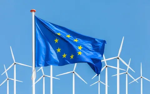 Europäische Flagge weht vor einer Reihe von Windrädern, die für erneuerbare Energien in der EU stehen.