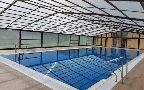 Una piscina cubierta con techo transparente y paredes de cristal, ideal para disfrutar todo el año. Estos porches para piscinas ofrecen un espacio acogedor.