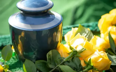 Niebieska urna pogrzebowa obok bukietu żółtych róż, kwiatów symbolizujących śmierć i pożegnanie.