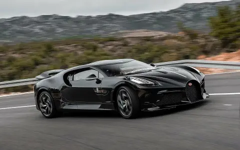 Czarny Bugatti La Voiture Noire pędzi po krętej drodze, otoczony przez górzysty krajobraz.