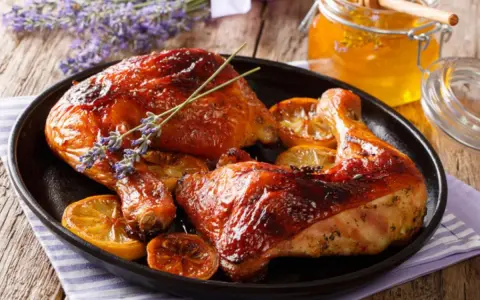 Muslos de pollo al horno dorados, servidos con rodajas de limón y un tarro de miel.