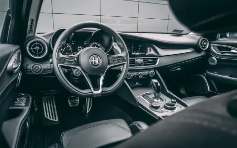 Wnętrze luksusowego samochodu Alfa Romeo. Kierownica, deska rozdzielcza i dźwignia zmiany biegów. Ta fotografia samochodowa oddaje styl i komfort.