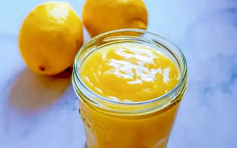 Un pot de lemon curd sans maïzena, onctueux et doré, à côté de deux citrons frais. Parfait pour une touche acidulée.