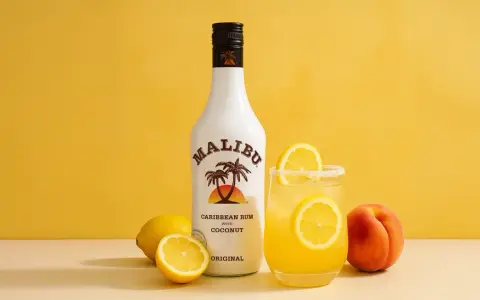 Malibu z mlekiem czy Malibu z sokiem ananasowym? Obok butelki białego rumu Malibu i drinka z cytryną stoi brzoskwinia.
