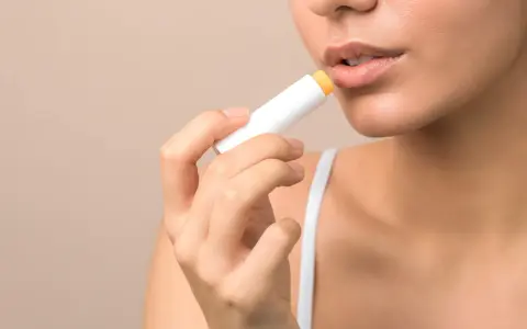 Kobieta aplikuje pomadkę ochronną na usta. Codzienna pielęgnacja ust to klucz do ich zdrowia i pięknego wyglądu.