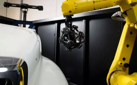 Robotyka i zaawansowany skaner optyczny badają kształt białego elementu, prawdopodobnie części samochodu.