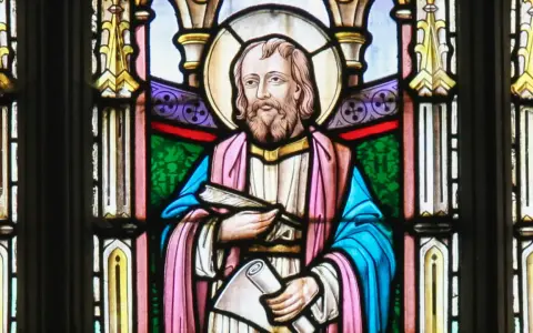 Witraż przedstawia świętego Łukasza z księgą i zwojem, symbolizując jego rolę jako ewangelisty i pisarza.