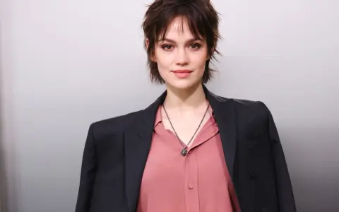 Junge Frau mit modischer Kurzhaarfrisur, inspiriert von Frisuren ab 50. Sie trägt einen rosafarbenen Blusen- und dunklen Blazer-Look.