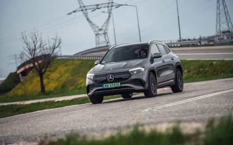 Szary Mercedes-Benz EQA jedzie po drodze, w tle linie energetyczne i drzewo.